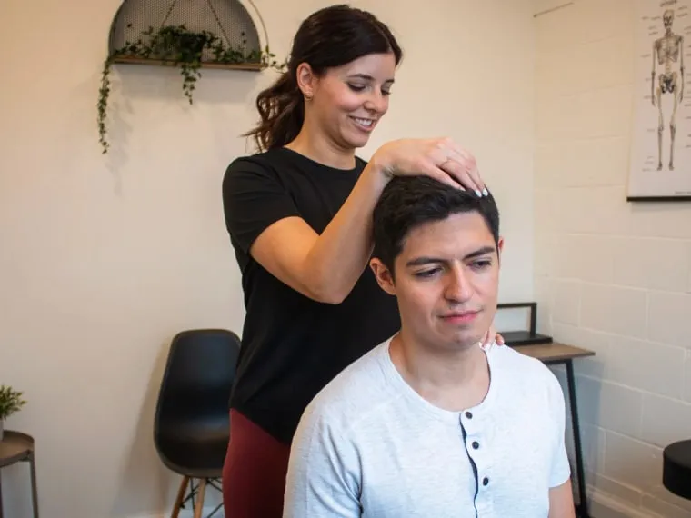 A chiropractor assessing the neck of a seated patient in a treatment room.